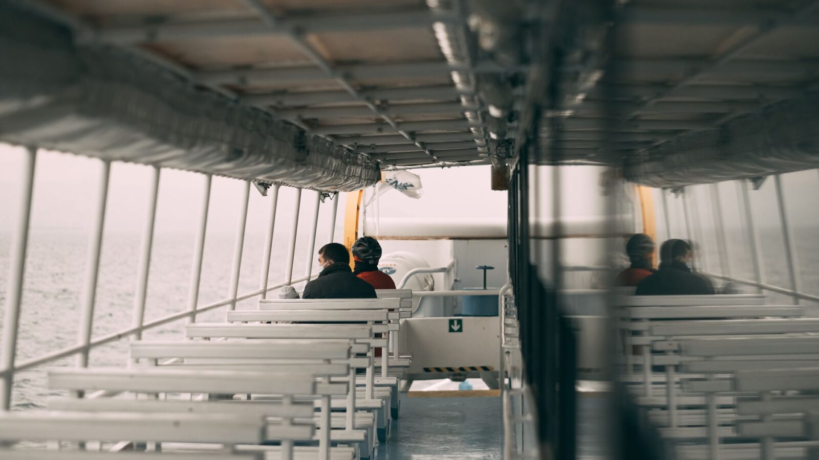 Two people enjoy a quiet ride on an empty ferry with a view of the sea.