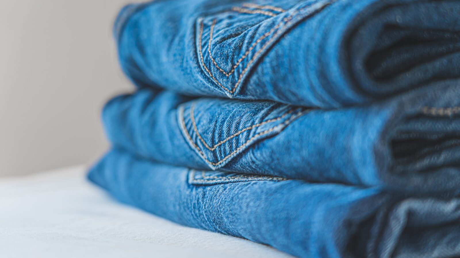 Close-up of neatly folded blue denim jeans on a white surface.