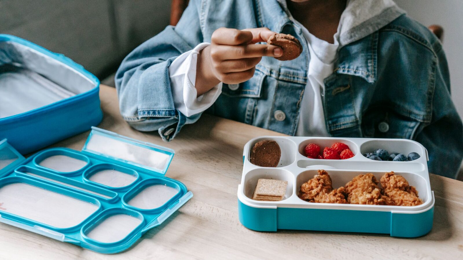 Crop anonymous African American boy eating cookies at table with container with berries
