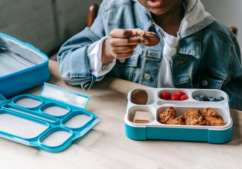 Crop anonymous African American boy eating cookies at table with container with berries